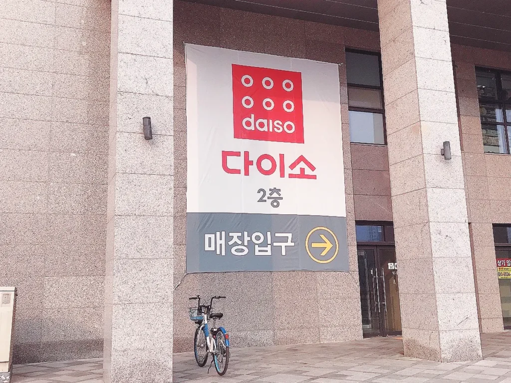 Entrance of a Daiso store in South Korea with a large white banner showing the red logo and 2nd-floor directions