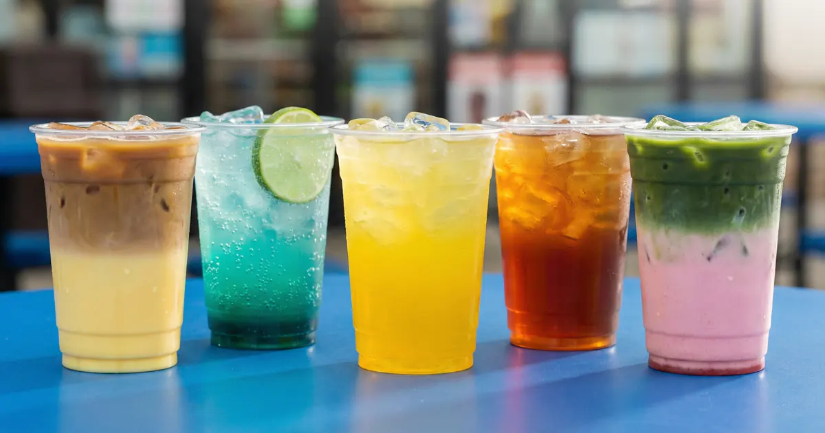 Five colorful DIY mocktail drinks in clear plastic cups lined up on a convenience store table in Korea, showcasing layered coffee, blue soda, yellow citrus soda, iced tea, and strawberry matcha combinations.