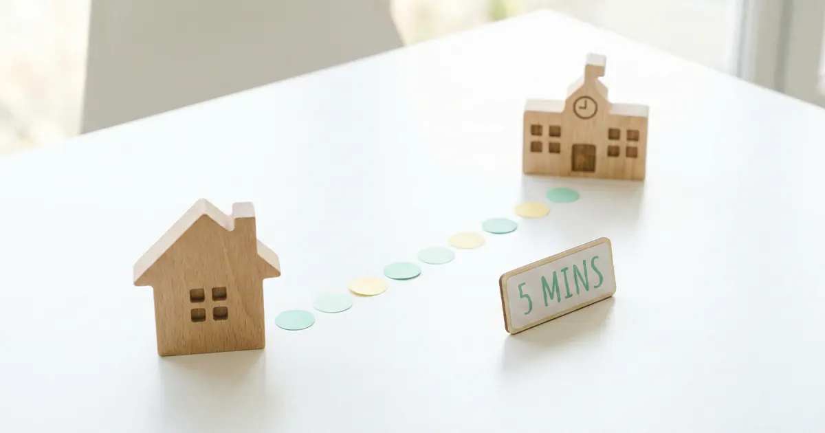 Miniature wooden models of a simple house and a school building on a white table connected by a path of colorful dots next to a sign that says 5 MINS.