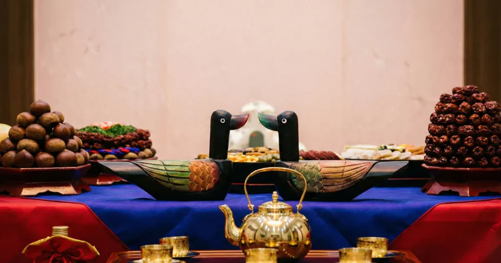A traditional Pyebaek table featuring a pair of colorful wooden mandarin ducks and a golden kettle on a red and blue cloth.