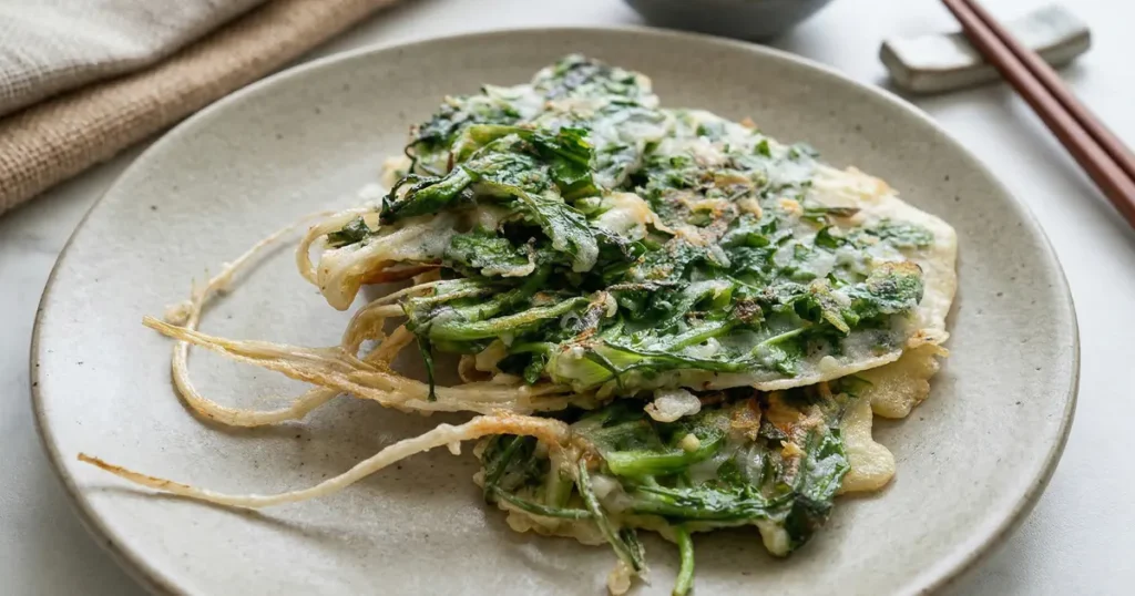 Golden brown Korean pancakes made with whole Naengi plants showing crispy green leaves and chewy white roots.